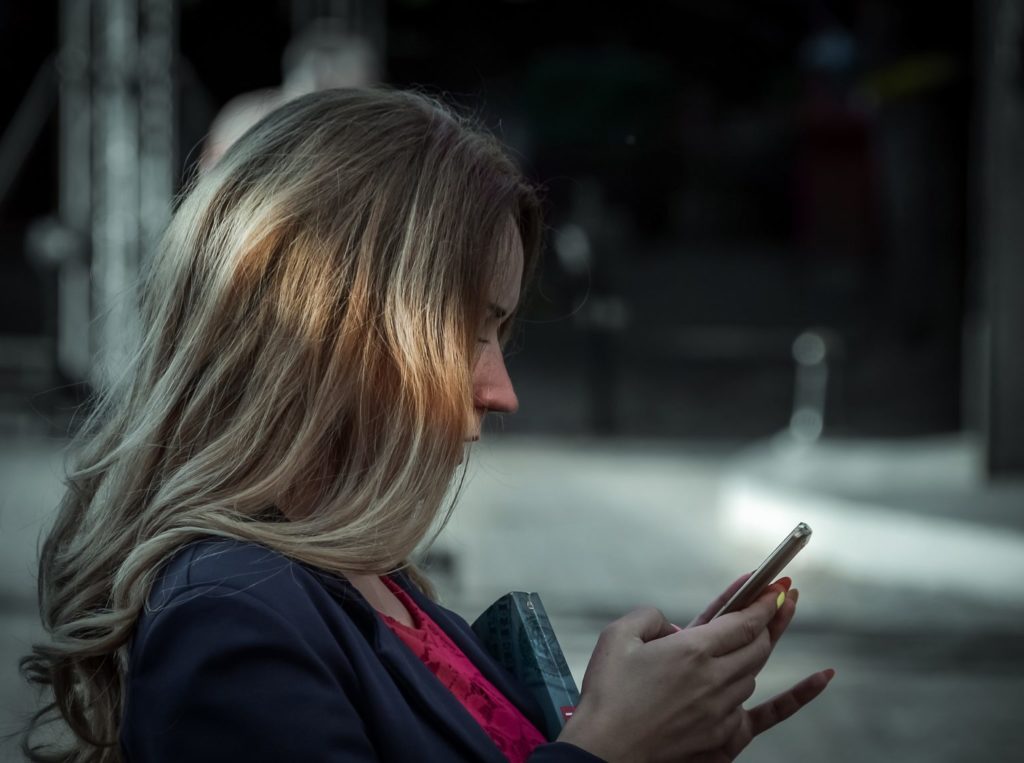 Eine blonde Frau schaut auf ihr Smartphone.