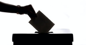 Ein Bild von einer Hand, die einen Briefumschlag in eine Wahlurne steckt.