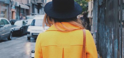 Person von hinten, trägt einen Hut und einen gelben Mantel