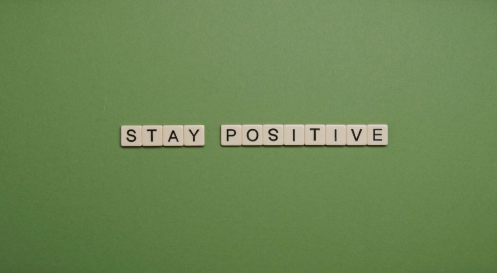 Stay Positive mit Scrabble-Steinen auf grünem Grund gelegt.
