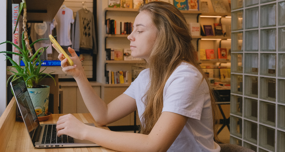 hateaid-digital-services-act-c-pexels-shvets-production Eine junge Frau am Laptop hält ihr Smartphone in der Hand.