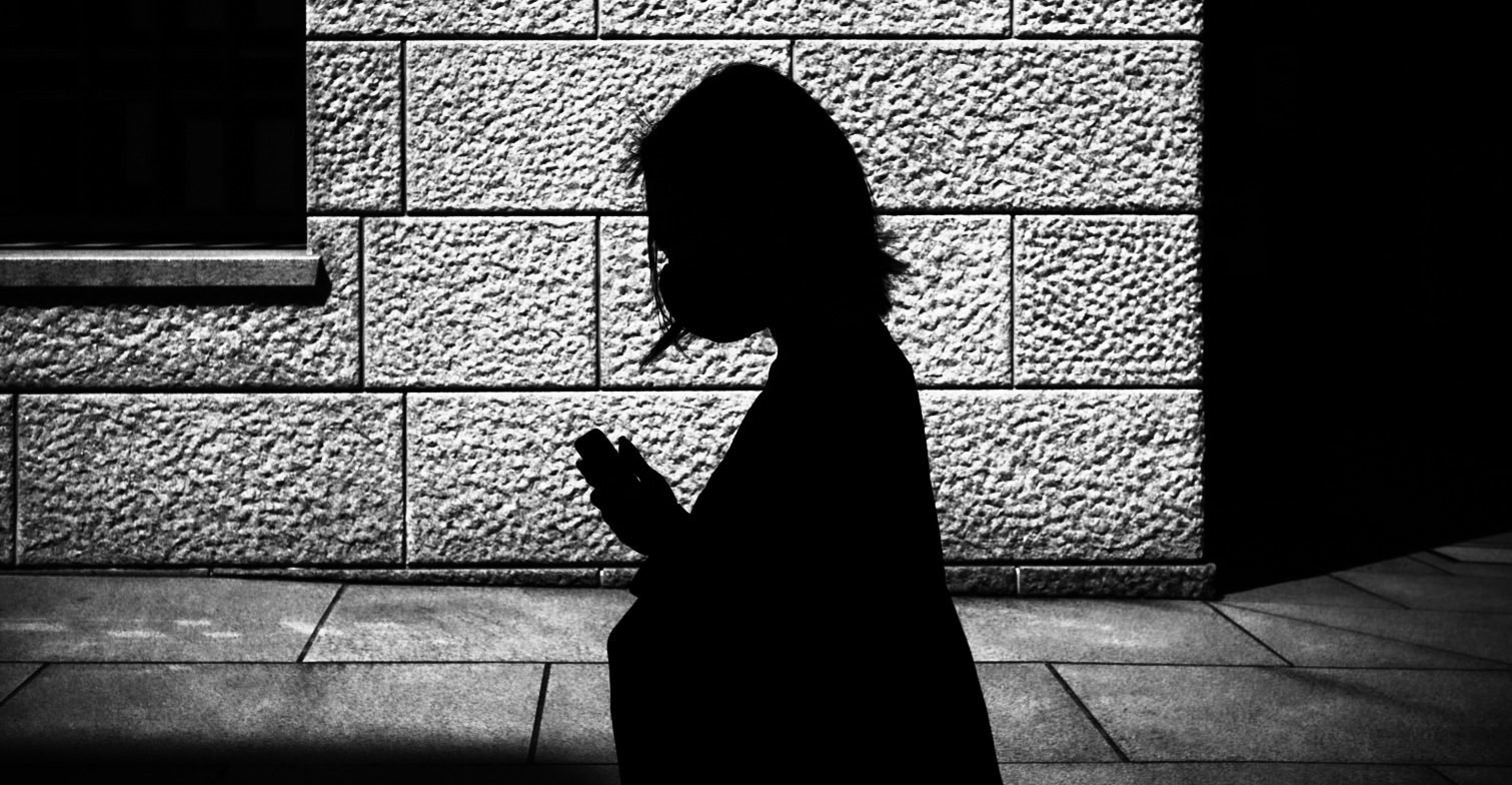 Eine Frau, deren Umrisse im Dunkeln erkennbar sind. Sie hält ein Smartphone in der Hand.