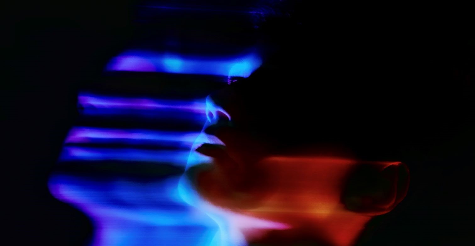 Digitale Gewalt: Deepfakes. Gesicht auf dunklem Hintergrund. Gesicht verschwimmt leicht in hellblau leuchtenden Farben.