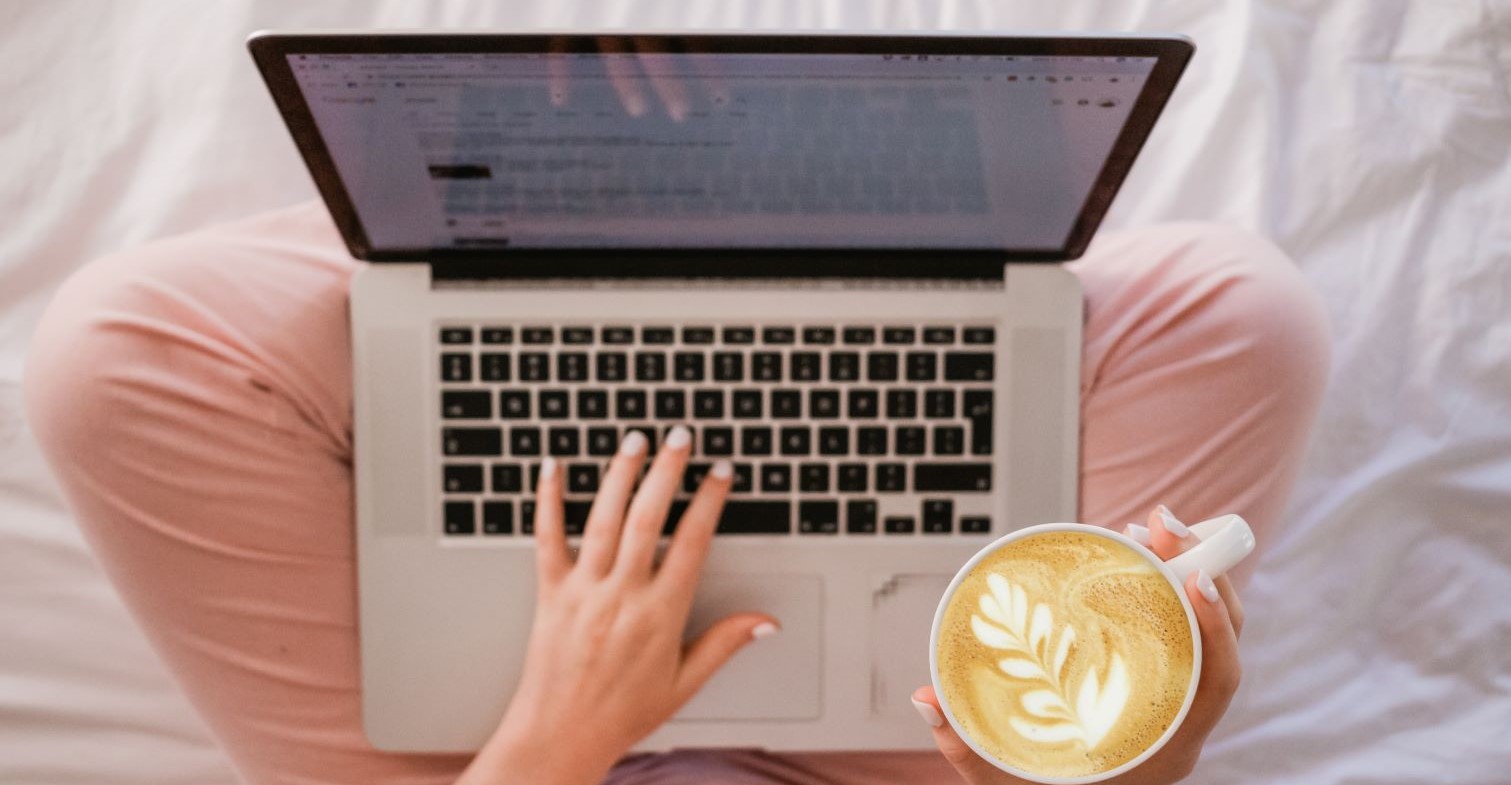 Person sitzt am Laptop mit Kaffee in der Hand.