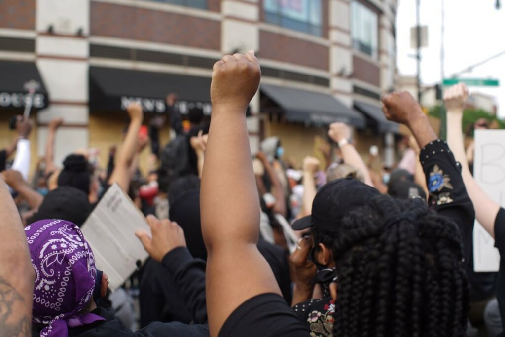 Bild einer protestierenden Menge mit Persons of Color, die die Faust aktivistisch hochrecken.