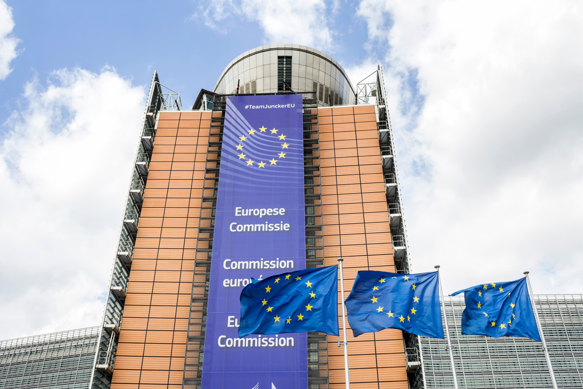 Foto vom Gebäude der Europäischen Kommission mit drei EU-Flaggen im Vordergrund.