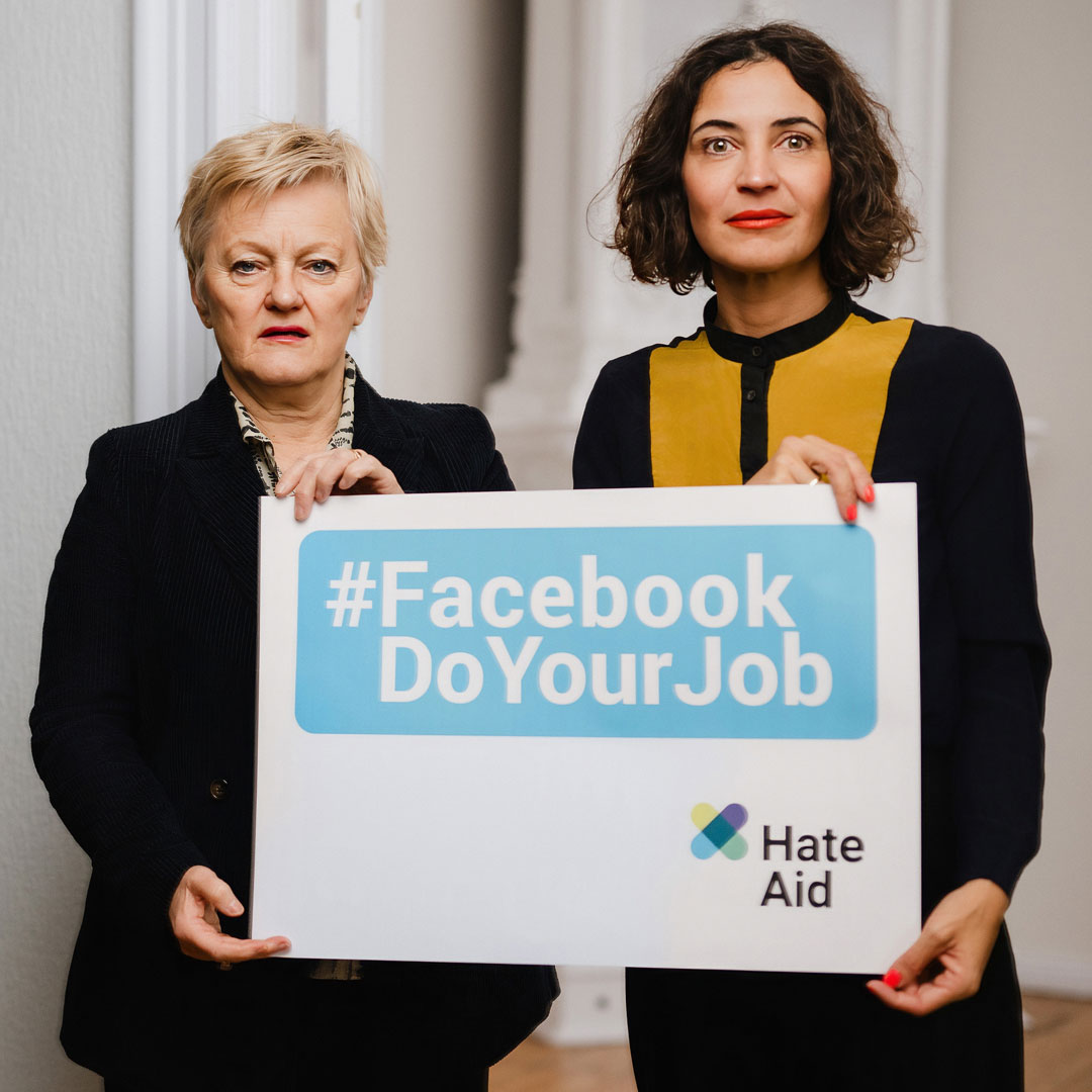 Bundestagsabgeodnete Renate Künast und HateAid-Geschäftsführerin Anna-Lena von Hodenberg halten ein Schild mit dem HateAid-Logo, auf dem #FacebookDoYourJob steht