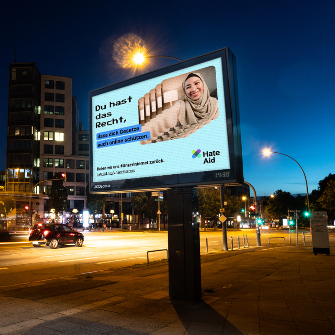 HateAid Menschenrechtskampagne #UnserInternet. Zu sehen ist ein Foto einer Straße bei Nacht und ein digitaler Werbebildschirm der Firma Wall GmbH. Copyright: Wall GmbH