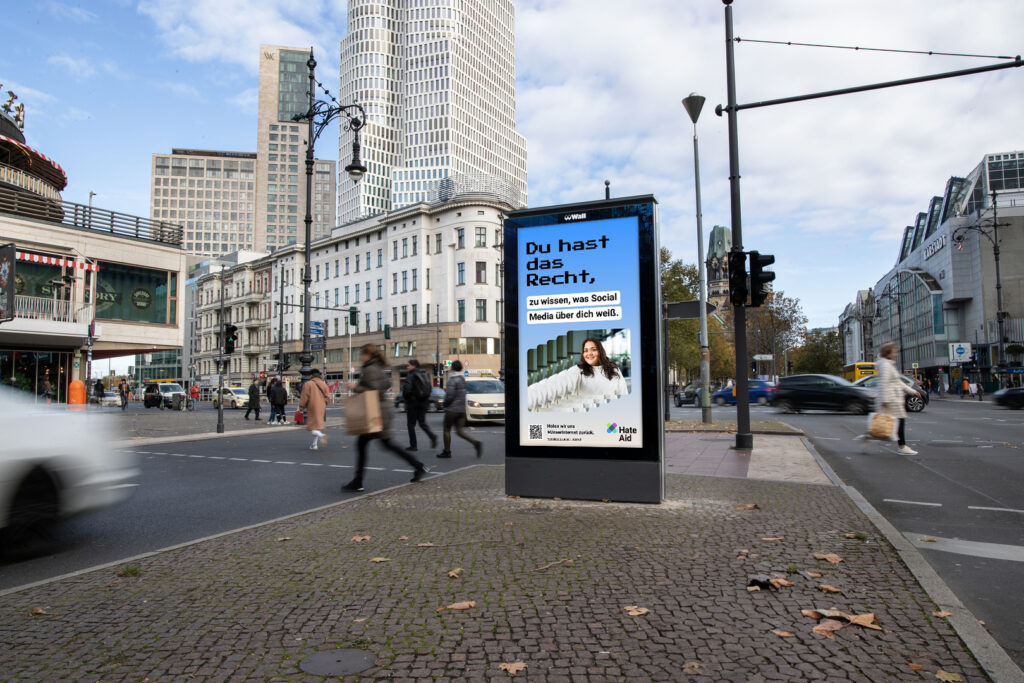 HateAid Menschenrechtskampagne #UnserInternet. Zu sehen ist ein Foto einer belebten Straße und ein Werbebildschirm der Firma Wall GmbH. Copyright: Wall GmbH