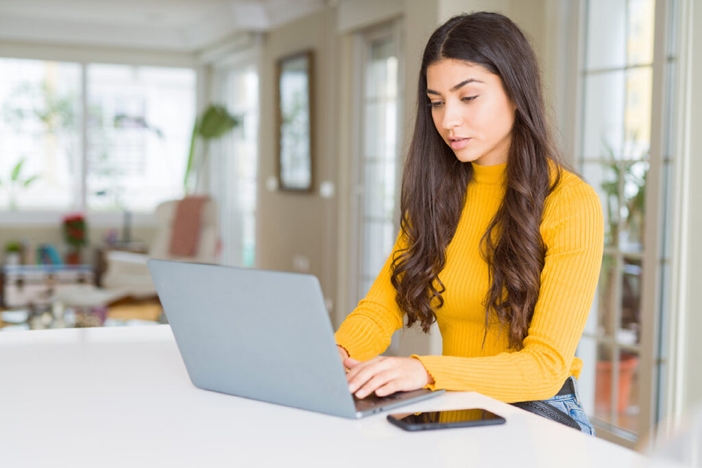Google Suchmaschine Suchergebnisse löschen lassen: Zu sehen ist eine Frau, die mit dem Laptop im Wohnzimmer am Tisch sitzt und tippt. Copyright: Shutterstock / Krankenimages.com
