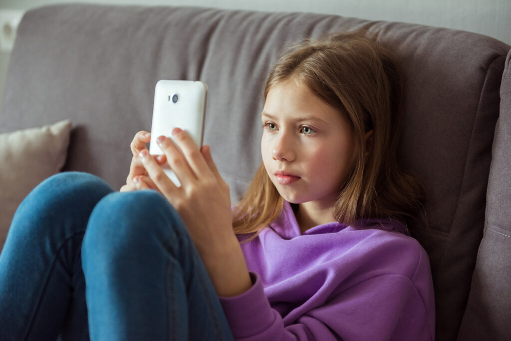 Internet kindersicher machen für Kinder und Jugendliche. Zu sehen ist ein Kind, sitzend auf dem Sofa mit Smartphone in der Hand.