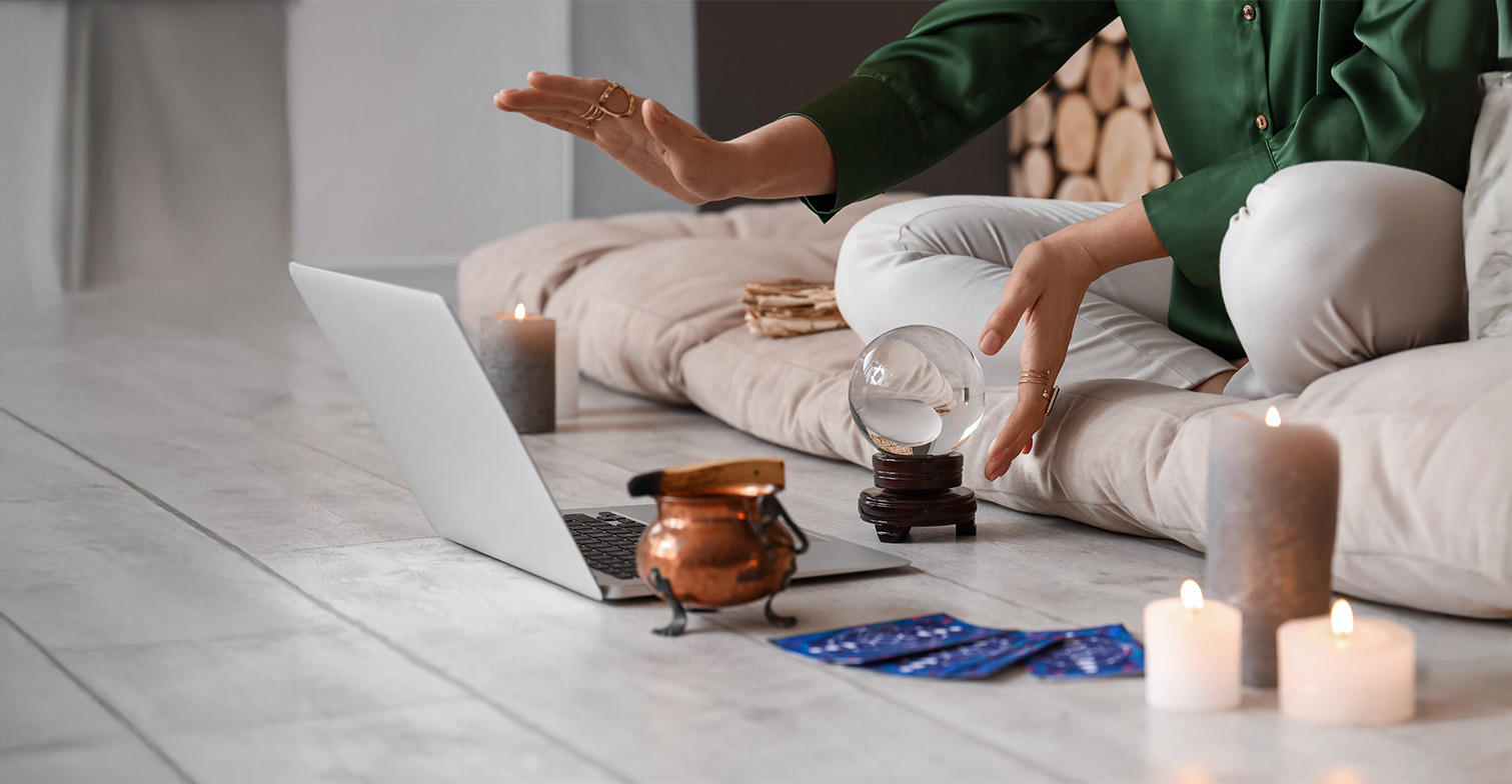 Bild von einer Person vor einem Laptop mit spirituellen Gegenständen um sich rum.